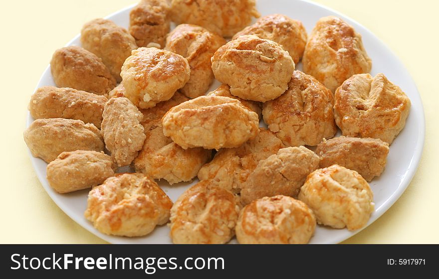 Close-up of crisp almond buns on a white plate, pale yellow background.