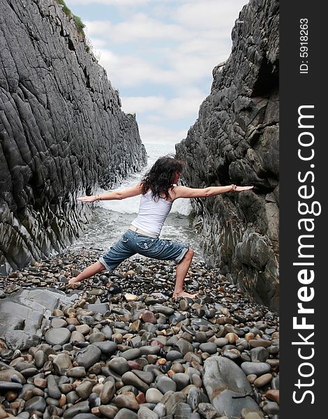 A beautiful woman practicing her yoga on the rocks in a ravine as the waves roll in. A beautiful woman practicing her yoga on the rocks in a ravine as the waves roll in