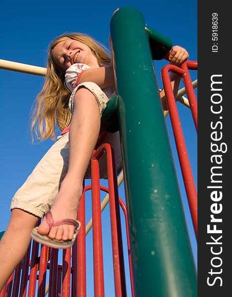 Young smiling girl playing in a playground with the blue sky in the background. Young smiling girl playing in a playground with the blue sky in the background.