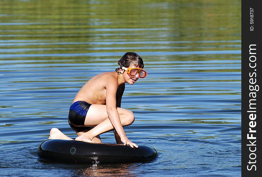 The boy with a diving mask kneeling down on a tube in a lake. The boy with a diving mask kneeling down on a tube in a lake.