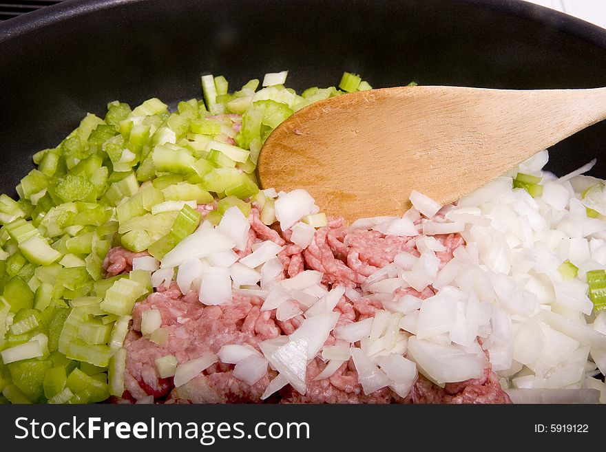 Meat, onions, and celery in a pan with a wooden spoon. Meat, onions, and celery in a pan with a wooden spoon