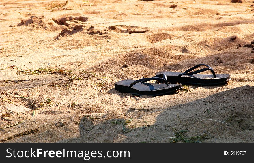 A pair of black slippers in the sand. A pair of black slippers in the sand.