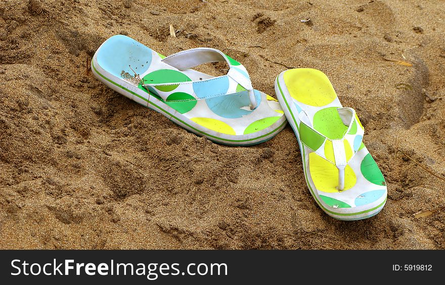 A pair of polka dotted flip flops in the sand.