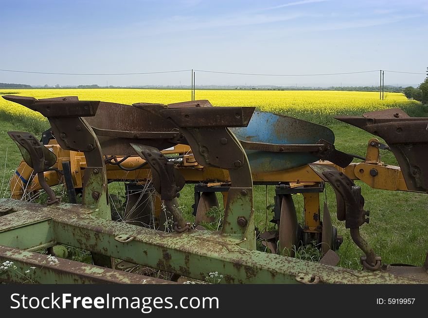 This rusting old plough is set against a vivid yellow field of oilseed rape and a light summer sky. Copy space at top. This rusting old plough is set against a vivid yellow field of oilseed rape and a light summer sky. Copy space at top.
