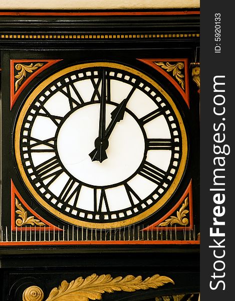 A large decorative station clock [ Charing Cross, London] with Roman numerals in black, gold and red.