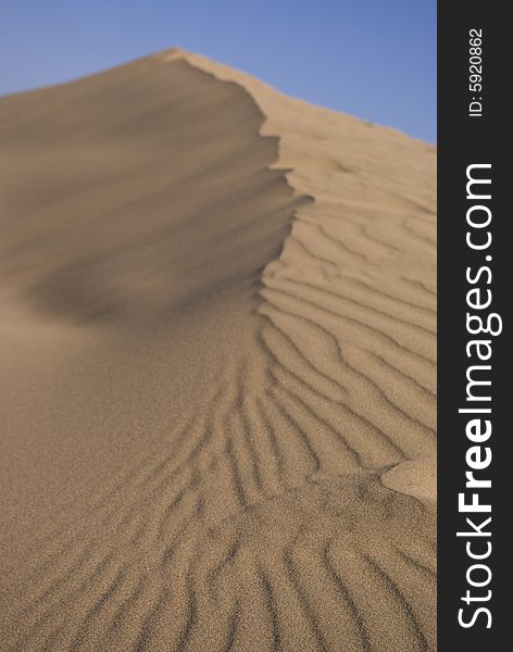 Desert sand dunes beneath a clear blue sky