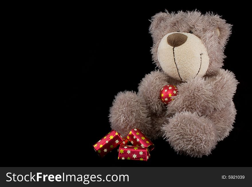 A grey cute teddy bear with sweets, isolated on black