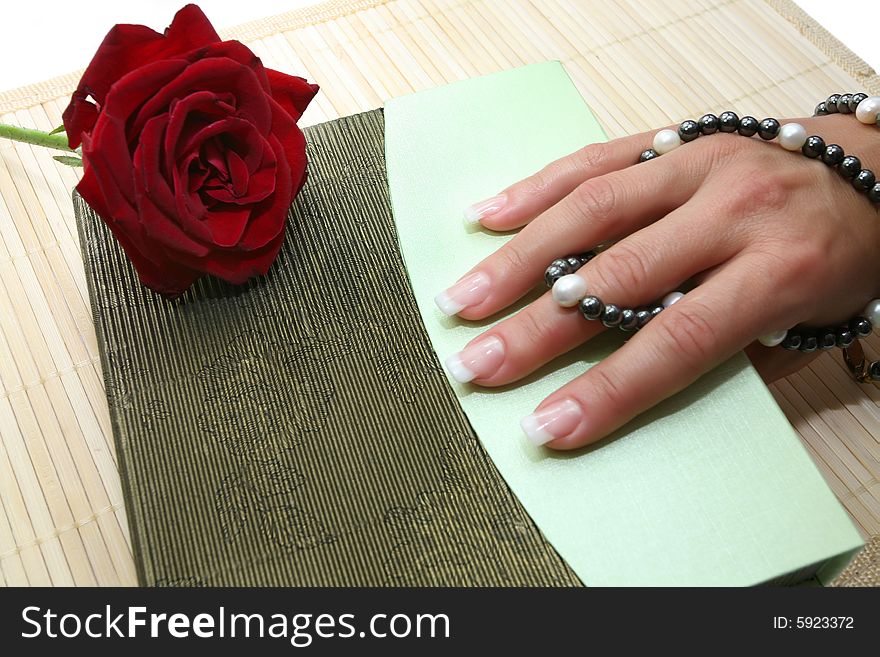 Beautiful long fingers with a good manicure hold beads from black and white pearls and a red rose lies alongside