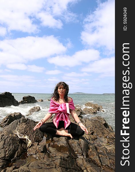 Beautiful woman meditating on the rocks in ireland with her eyes closed, in the lotus position, showing a healthy way to live a happy and relaxed lifestyle in a world full of stress. Beautiful woman meditating on the rocks in ireland with her eyes closed, in the lotus position, showing a healthy way to live a happy and relaxed lifestyle in a world full of stress