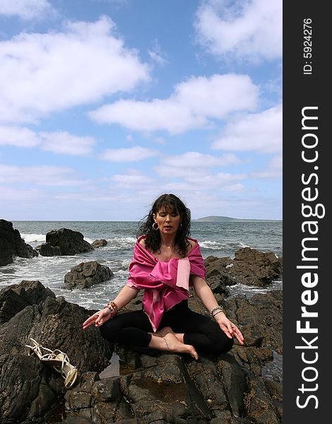 Beautiful woman meditating on the rocks in ireland with her eyes closed, in the lotus position, showing a healthy way to live a happy and relaxed lifestyle in a world full of stress. Beautiful woman meditating on the rocks in ireland with her eyes closed, in the lotus position, showing a healthy way to live a happy and relaxed lifestyle in a world full of stress