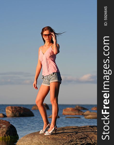 Young girl standing near the sea and touches her sunglasses