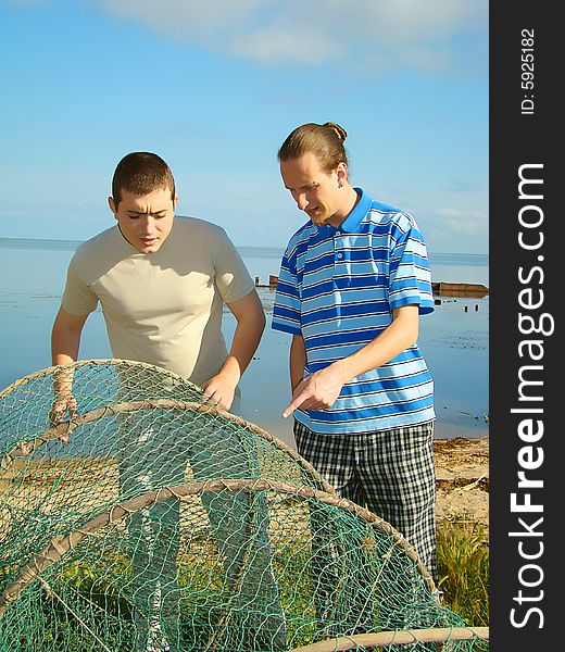 Two young adult men examine a fishing net on the riverside. Two young adult men examine a fishing net on the riverside.