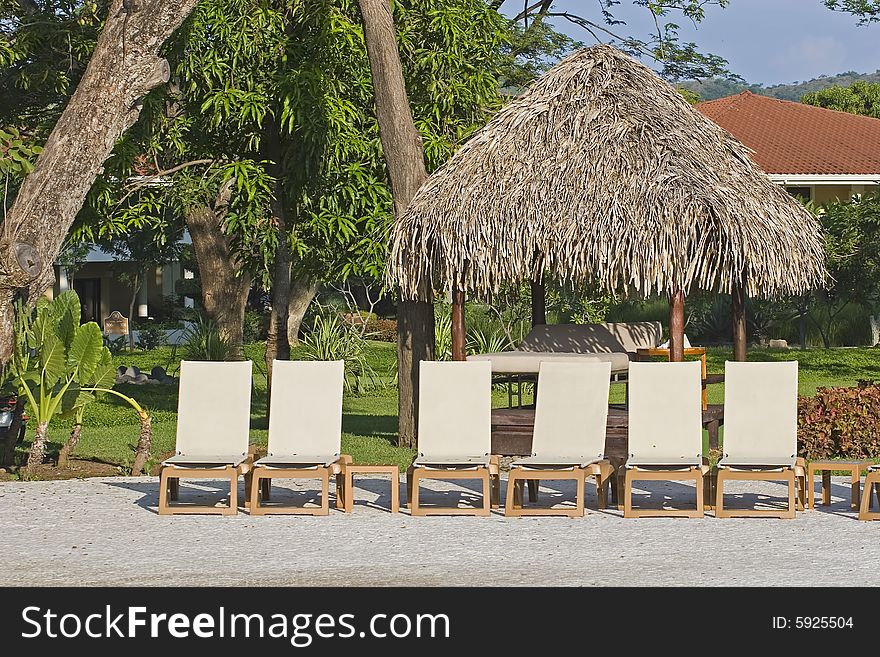 White lounge chairs and a straw hut around a tropical swimming pool. White lounge chairs and a straw hut around a tropical swimming pool