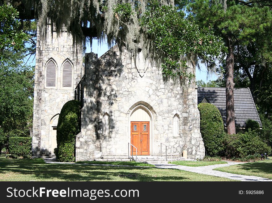 An old stone church sits behind trees with Spanish moss haning down.