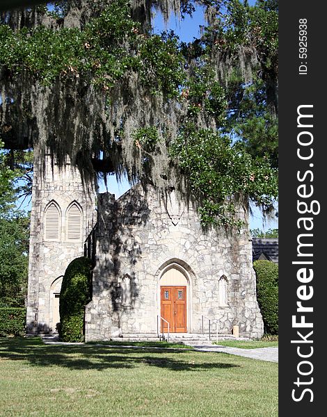 An old stone church sits behind trees with Spanish moss haning down.