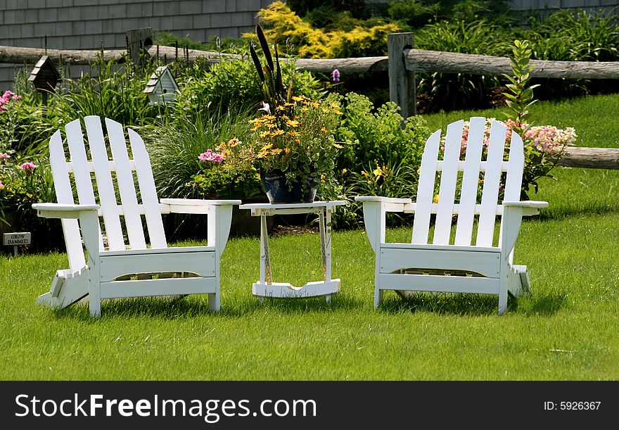 Two white adirondack chairs sit on the lawn ready for someone to sit and enjoy. Two white adirondack chairs sit on the lawn ready for someone to sit and enjoy.