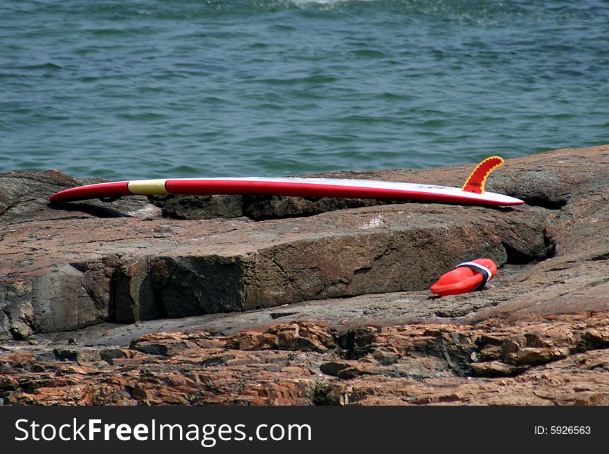 A surf board lays forgotten on the rocks until someone comes back for it.