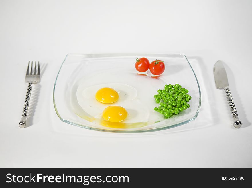Two raw egg yolk, two cherry tomato and green pees on a plate and isolated on a white background. Two raw egg yolk, two cherry tomato and green pees on a plate and isolated on a white background