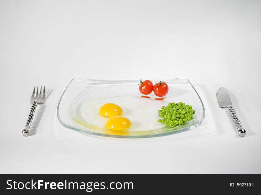 Two raw egg yolk, two cherry tomato and green pees on a plate and isolated on a white background. Two raw egg yolk, two cherry tomato and green pees on a plate and isolated on a white background