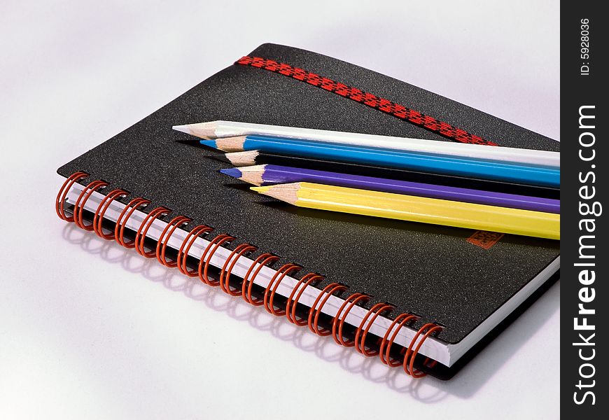 Black note book with colored pencils on white background.