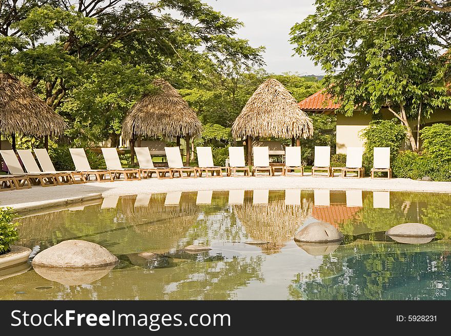 White chaise lounges around a tropical swimming pool. White chaise lounges around a tropical swimming pool