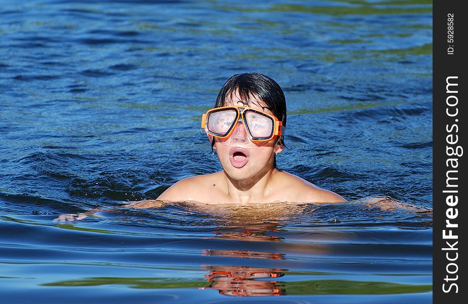 The boy with a misted diving mask swimming in a blue lake water. The boy with a misted diving mask swimming in a blue lake water.