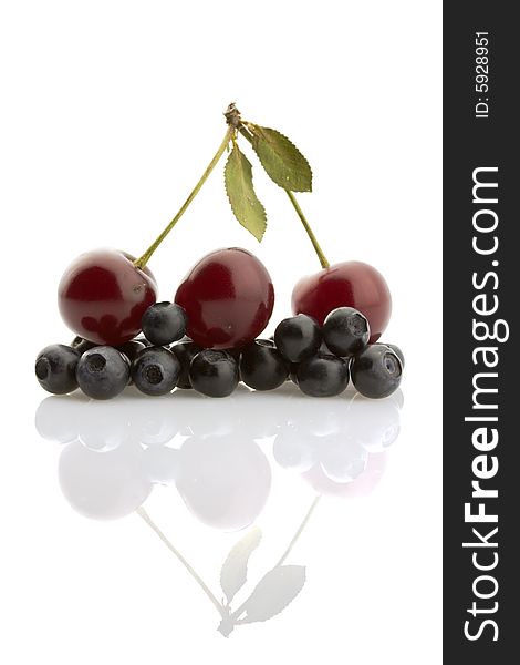 Ripe cherries and bilberries reflected on white background. Ripe cherries and bilberries reflected on white background