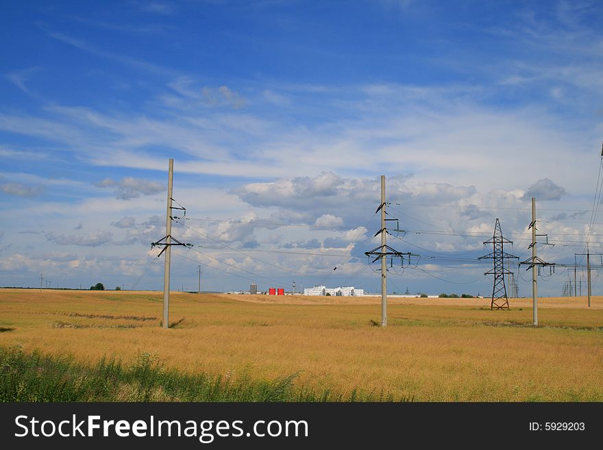 Yellow field under the dark blue sky on which buildings and electrosupport cost(stand)