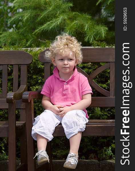 Cute young boy sitting on a bench in summer