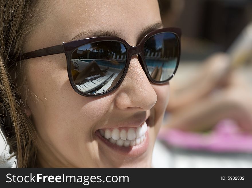 Happy young woman wearing sunglasses, with a reflextion of the pool. Happy young woman wearing sunglasses, with a reflextion of the pool.
