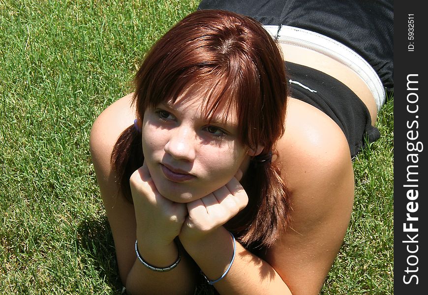 A picture of a teen girl with red hair and pigtails laying in the grass.