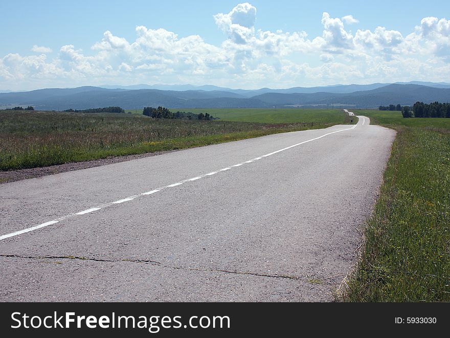 Landscape with the asphalted empty road, taking place waves on hills, clouds, the sky, mountains in distances. Beauty and calmness. Landscape with the asphalted empty road, taking place waves on hills, clouds, the sky, mountains in distances. Beauty and calmness.