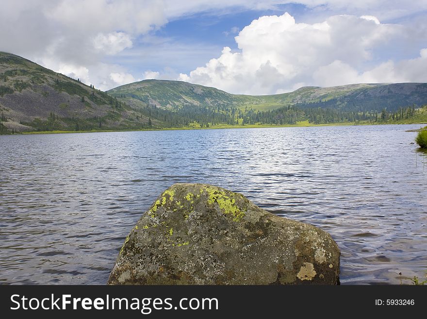 Kind on mountain lake. A stone with a lichen in the foreground.