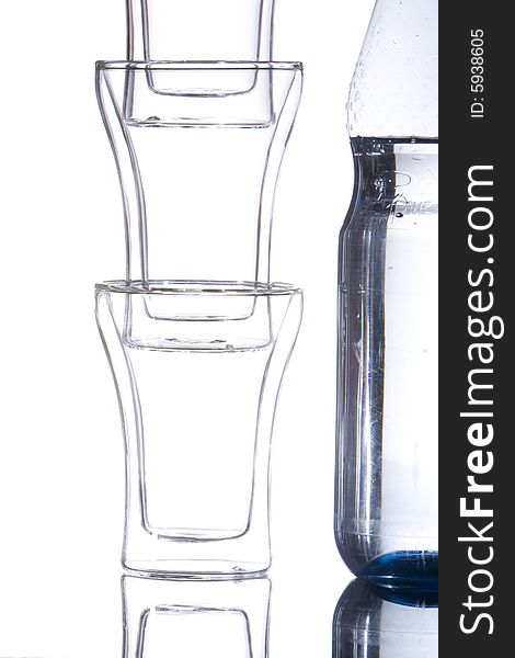 A bottle of mineralwater with three piled glasses.
