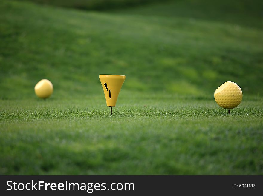 Close view of two yellow balls on a tee in front of a green background. Close view of two yellow balls on a tee in front of a green background