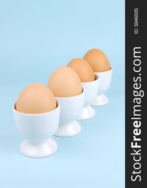 Hard boiled eggs in egg cups isolated against a blue background