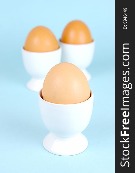 Hard boiled eggs in egg cups isolated against a blue background