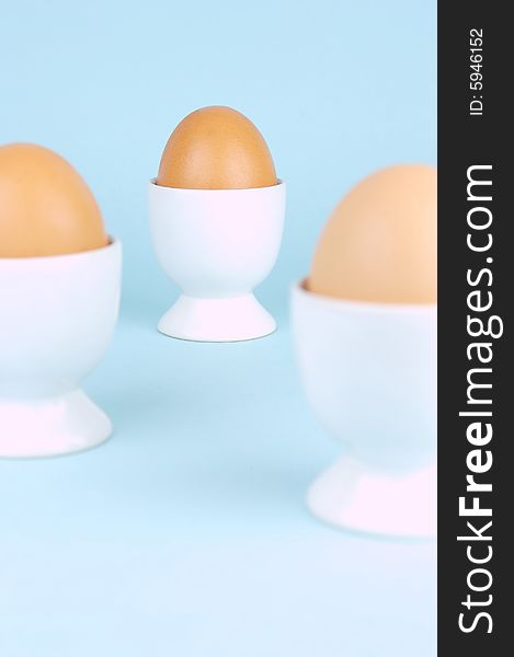 Hard boiled eggs in egg cups isolated against a blue background