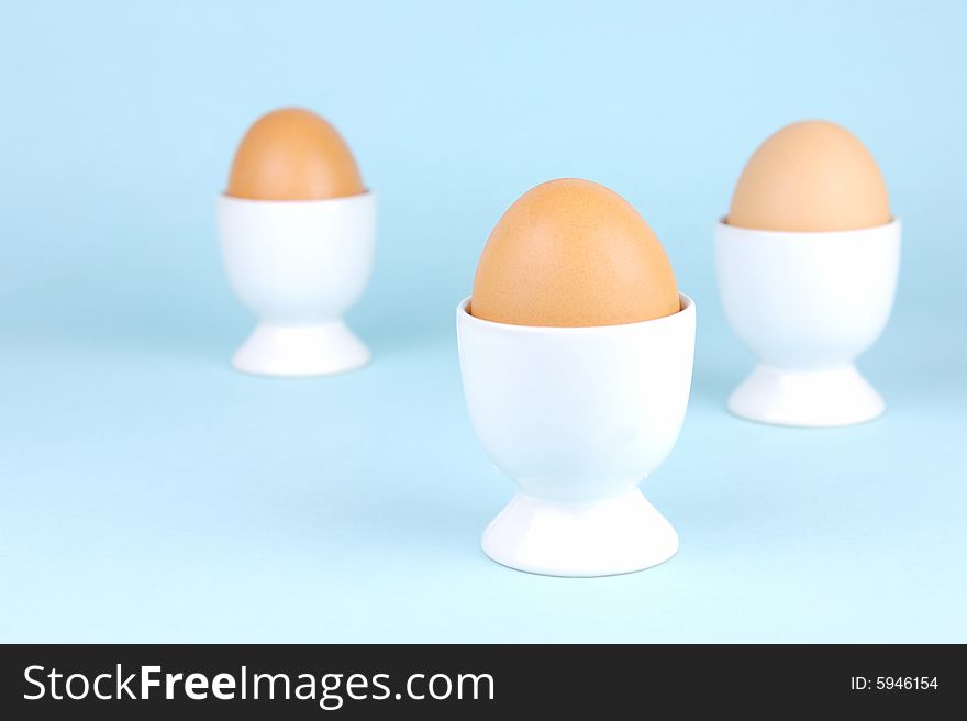 Hard boiled eggs in egg cups isolated against a blue background