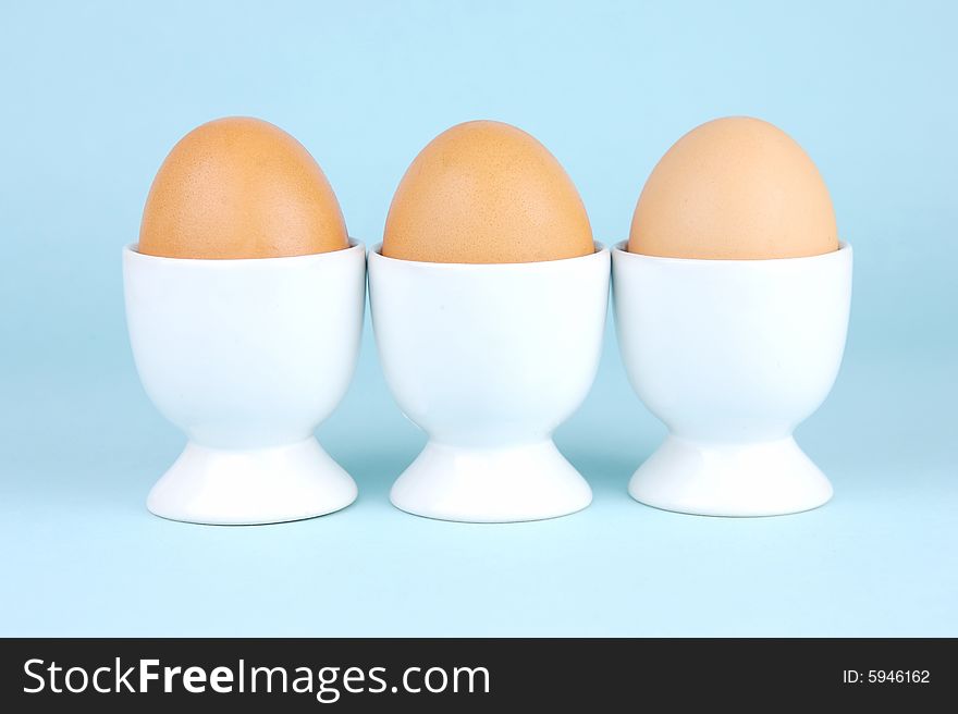 Hard boiled eggs in egg cups isolated against a blue background