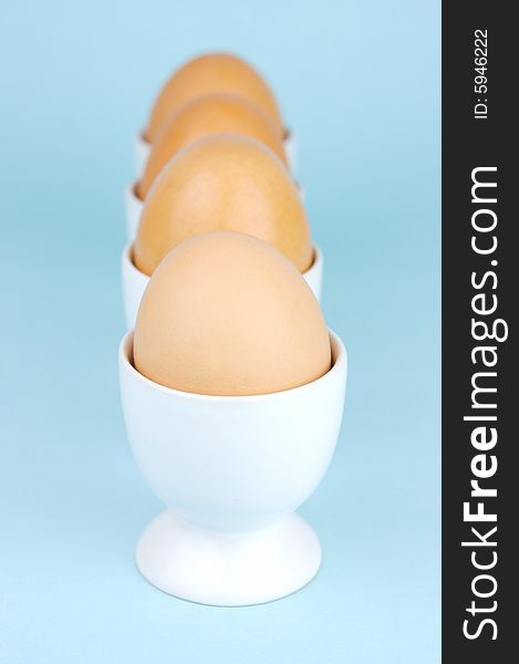 Hard boiled eggs in egg cups isolated against a blue background