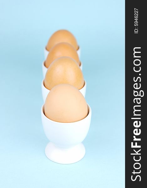 Hard boiled eggs in egg cups isolated against a blue background