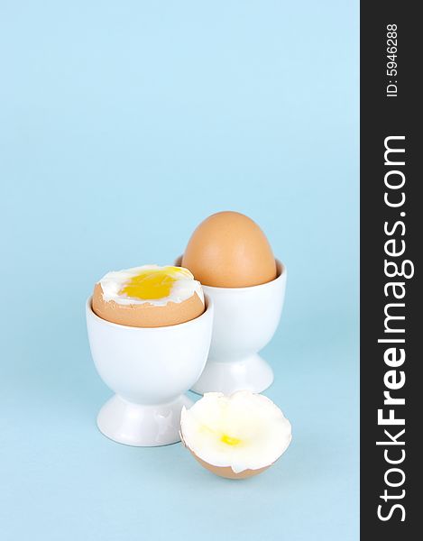 Hard boiled eggs in egg cups isolated against a blue background