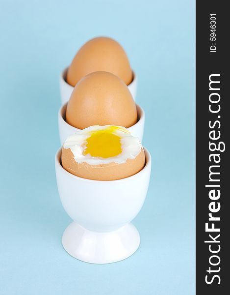 Hard boiled eggs in egg cups isolated against a blue background