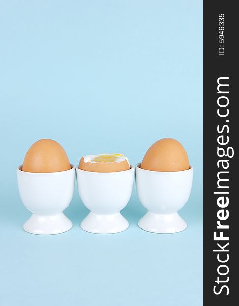 Hard boiled eggs in egg cups isolated against a blue background