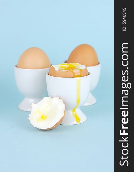 Hard boiled eggs in egg cups isolated against a blue background