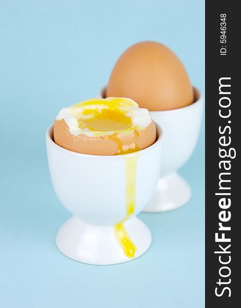 Hard boiled eggs in egg cups isolated against a blue background