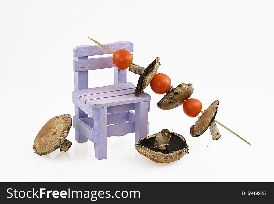 Composition from a mushroom shish kebab with tomatoes and a wooden decorative bench. Composition from a mushroom shish kebab with tomatoes and a wooden decorative bench