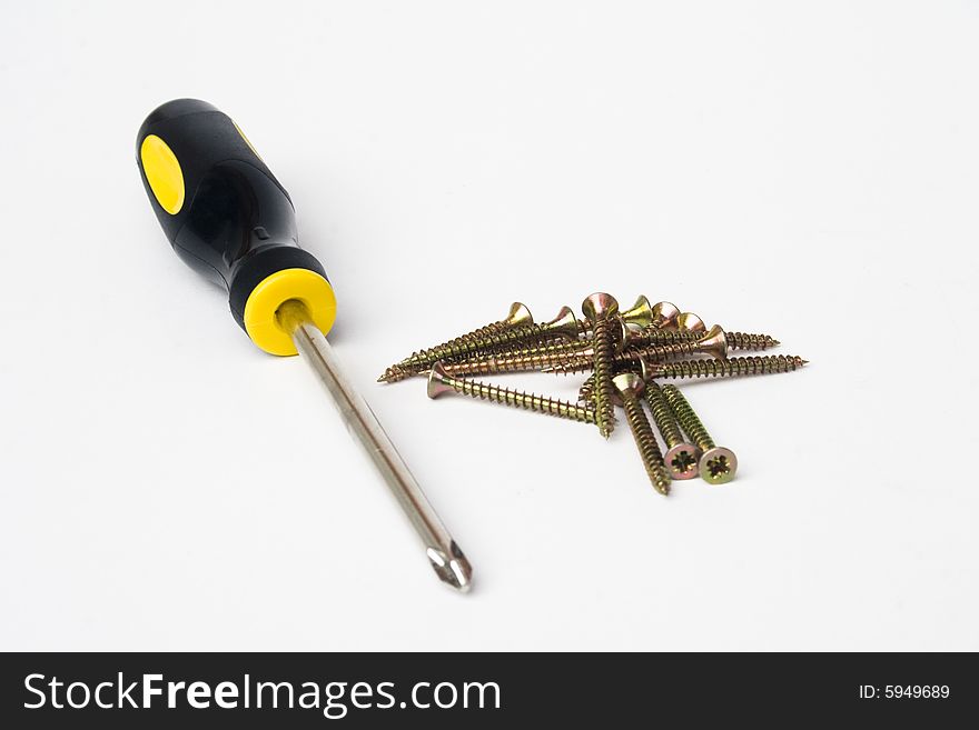 Yellow and black handled phillips screwdriver with pile of screws on white background. Yellow and black handled phillips screwdriver with pile of screws on white background