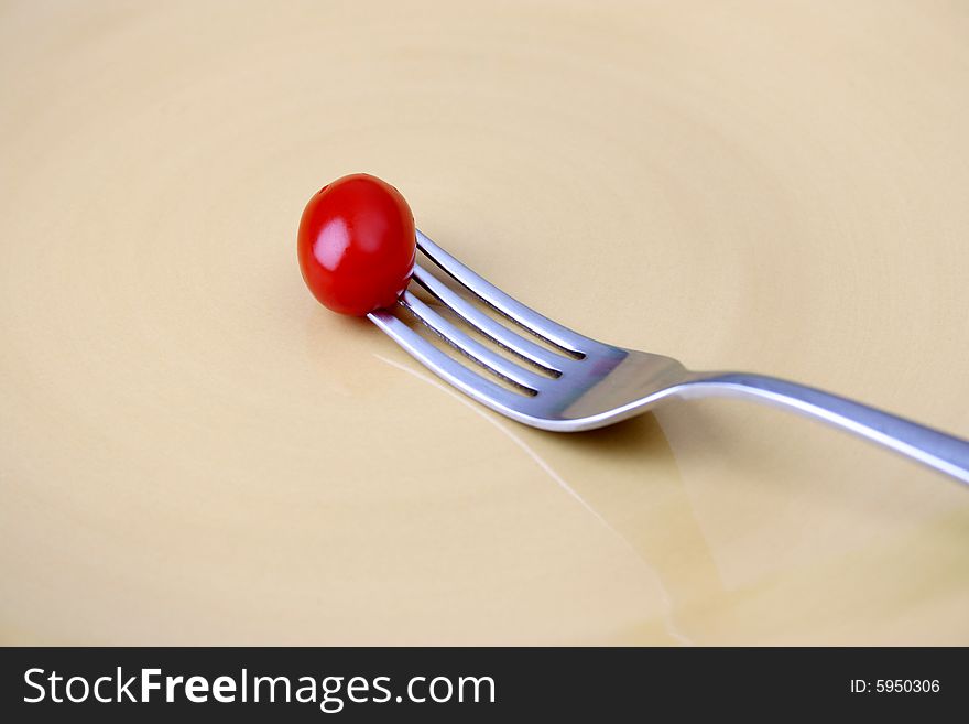Single tomato on a fork against a yellow plate. Single tomato on a fork against a yellow plate
